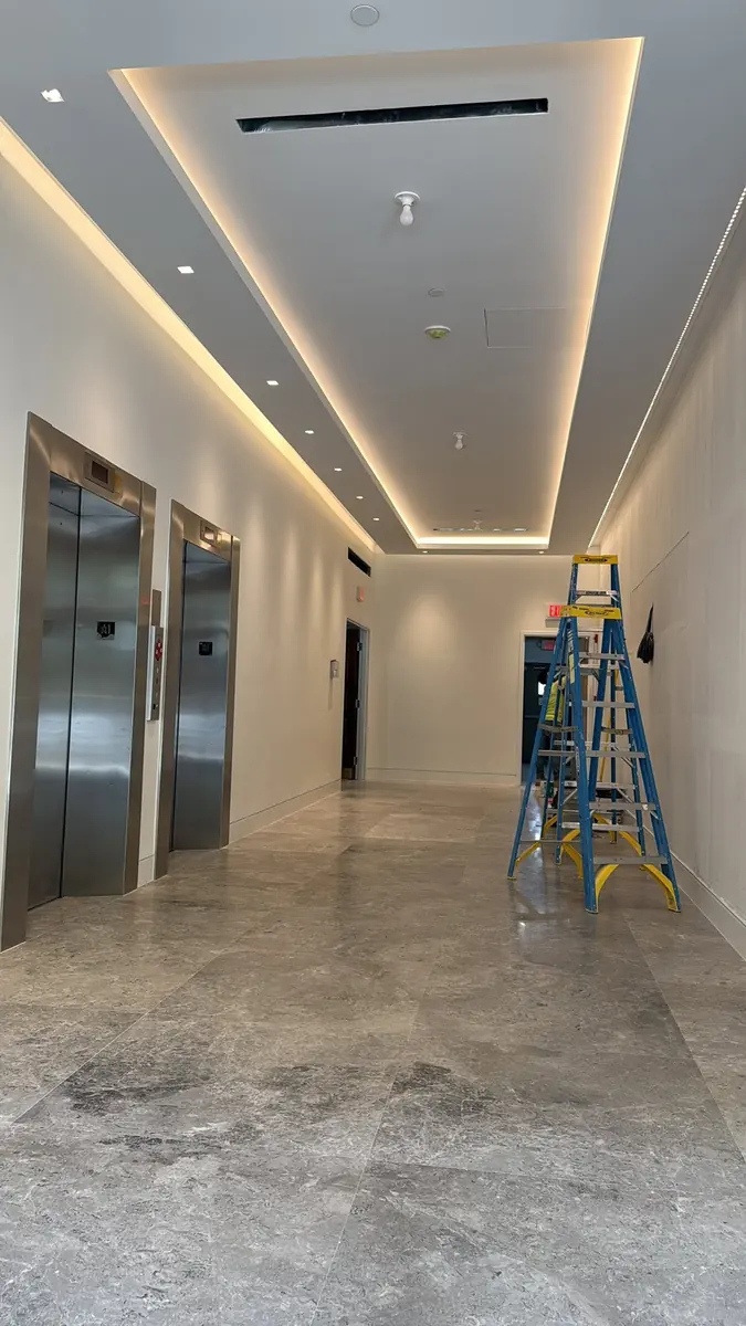 Building elevator lobby freshly painted, with cove lighting and stone floors, ladders on site