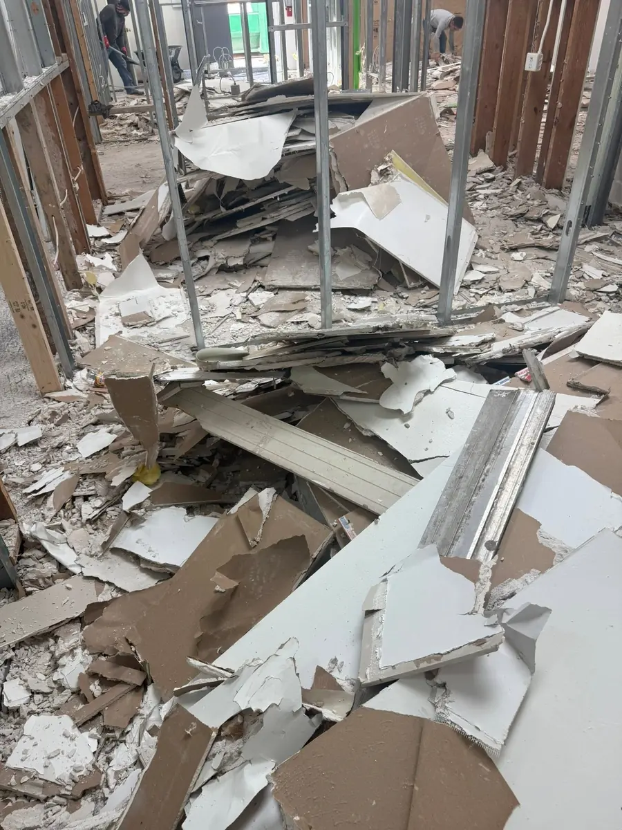 Crew removing drywall debris between exposed metal studs during a commercial demolition