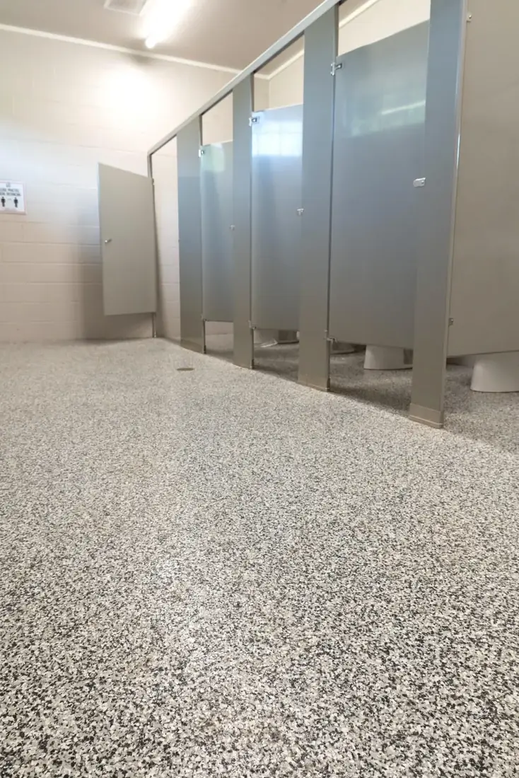 Commercial restroom with a gray decorative flake floor under the toilet partitions