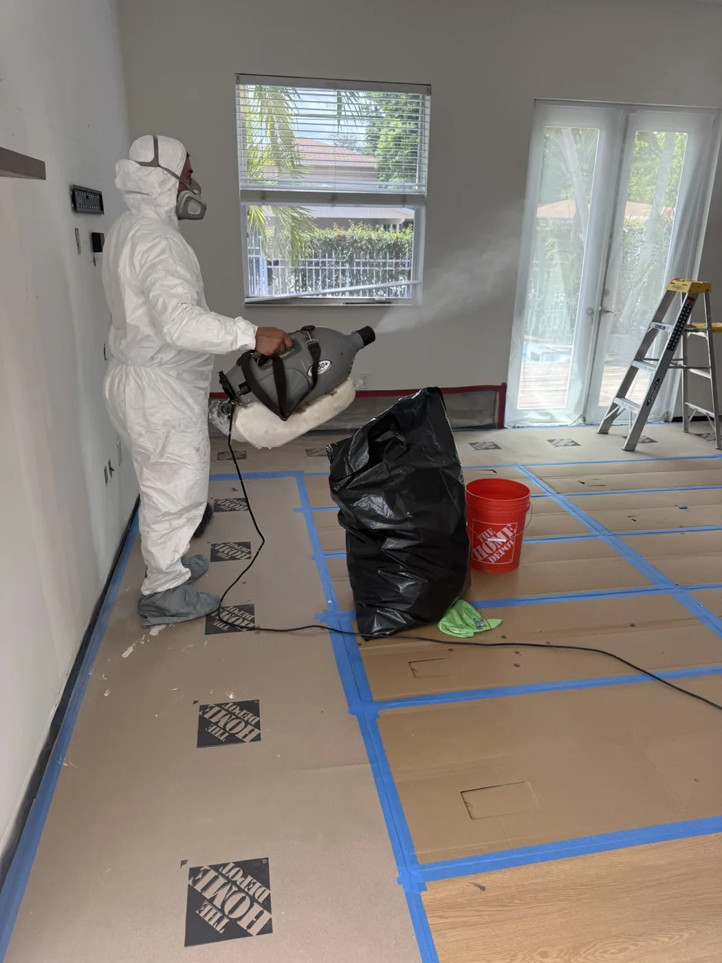 BO Restoration technician in a protective suit and respirator fogging a room with disinfectant, with floors covered and taped