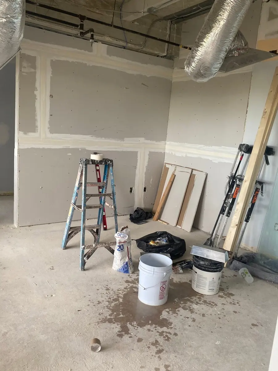 Drywall finishing in progress with joint compound, tape, ladder and drywall lifts on site
