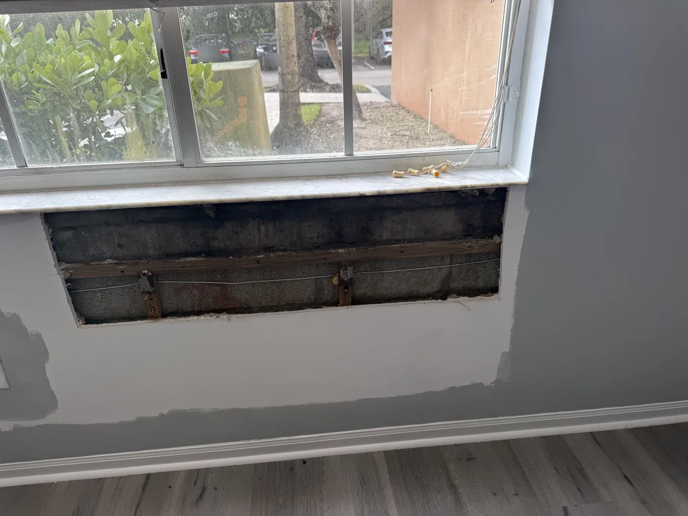 Drywall opening below a window during repair, with the surrounding wall patched and primed