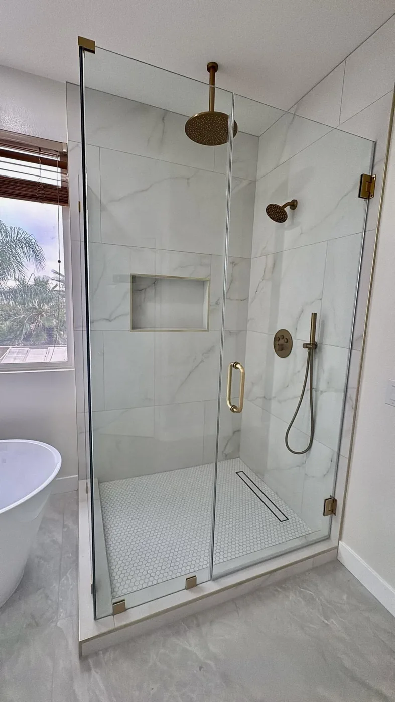 Frameless glass shower with marble-look porcelain tile, brushed gold fixtures, rain showerhead, linear drain and hexagon mosaic floor