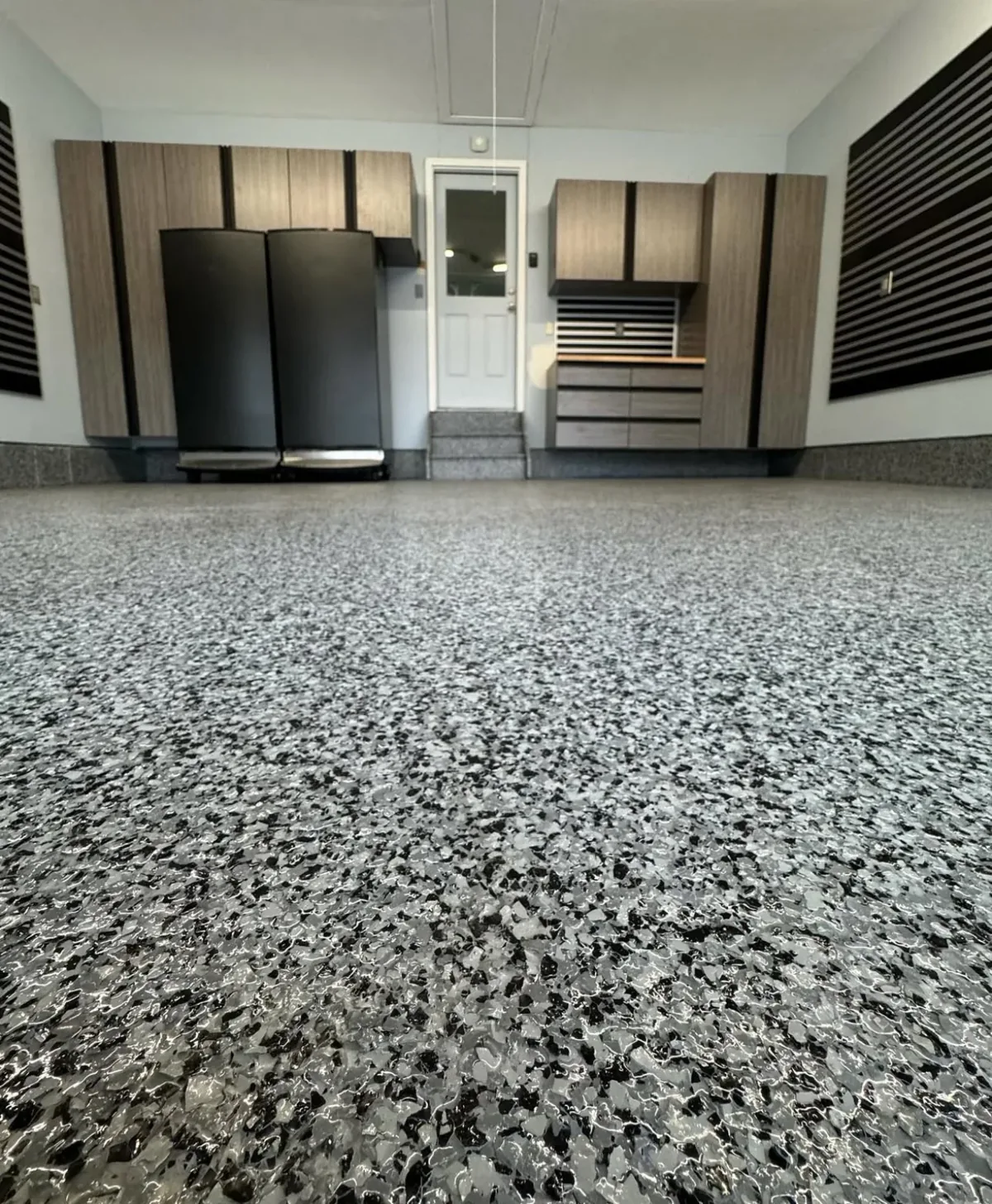 Garage floor with a gray and black full-broadcast flake coating, coved edges and coated steps, with storage cabinets