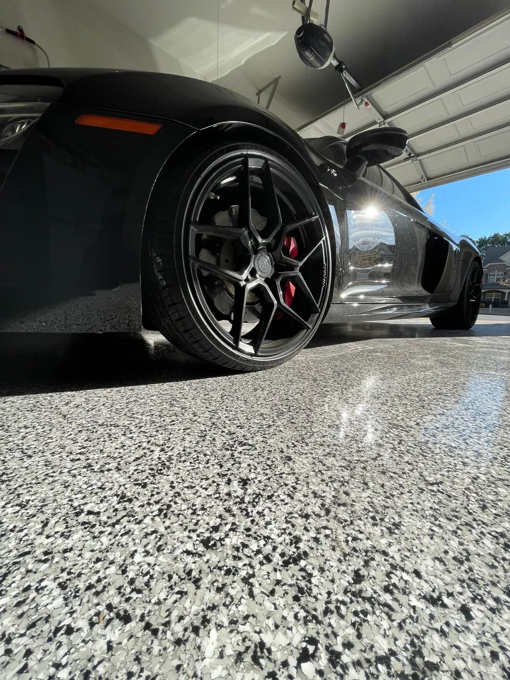 Glossy gray, black and white full-broadcast flake coating on a garage floor, with a black sports car parked on it