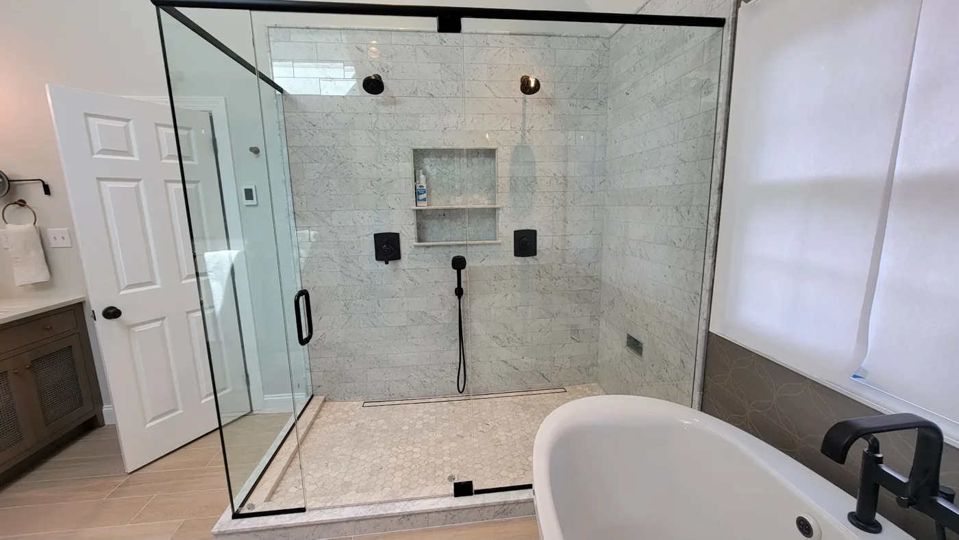 Large glass shower enclosure with marble subway tile, dual matte black showerheads, built-in niche and freestanding tub