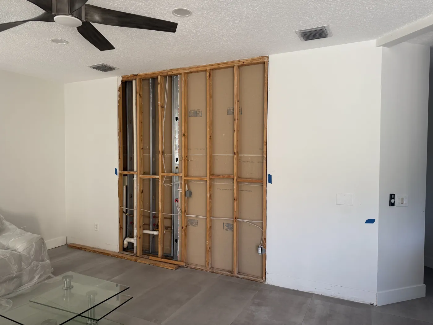 Living room wall opened to the studs during interior demolition, with furniture covered and floors protected