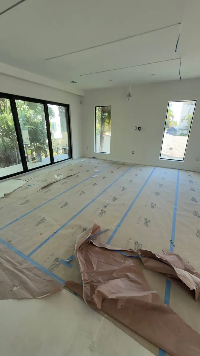 Freshly painted living area in a modern home with large windows, floors covered with taped protection paper