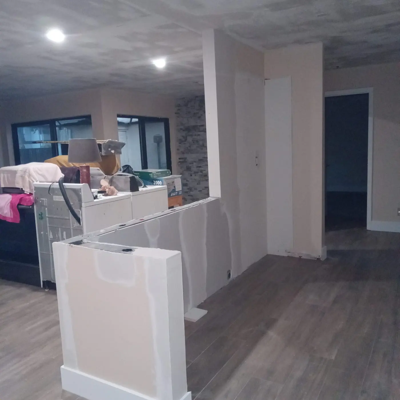 Kitchen area before the remodel, with a new half wall framed, drywalled and taped over the new wood-look tile floor