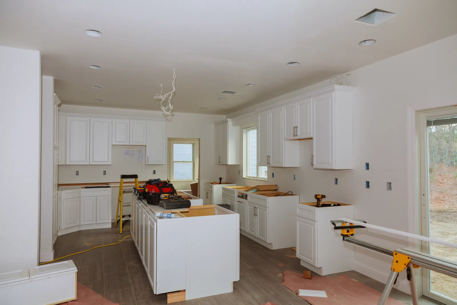 Kitchen remodel in progress: new white cabinets and island being installed, with tools and protected floors