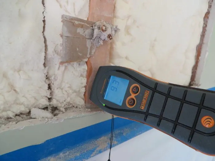 Moisture meter checking an opened wall cavity with foam insulation after water damage