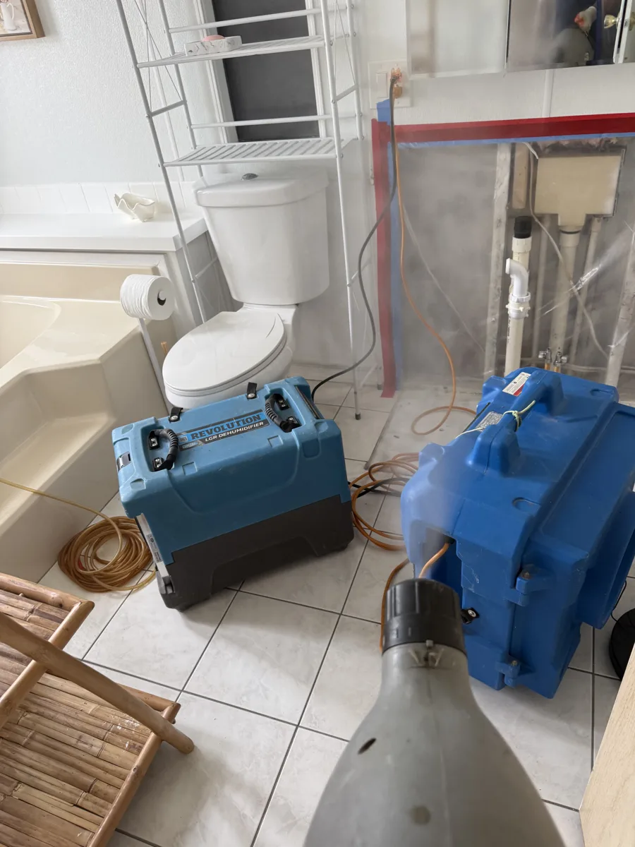 Plastic containment taped over the opened wall, with an LGR dehumidifier and a HEPA air scrubber running in the bathroom