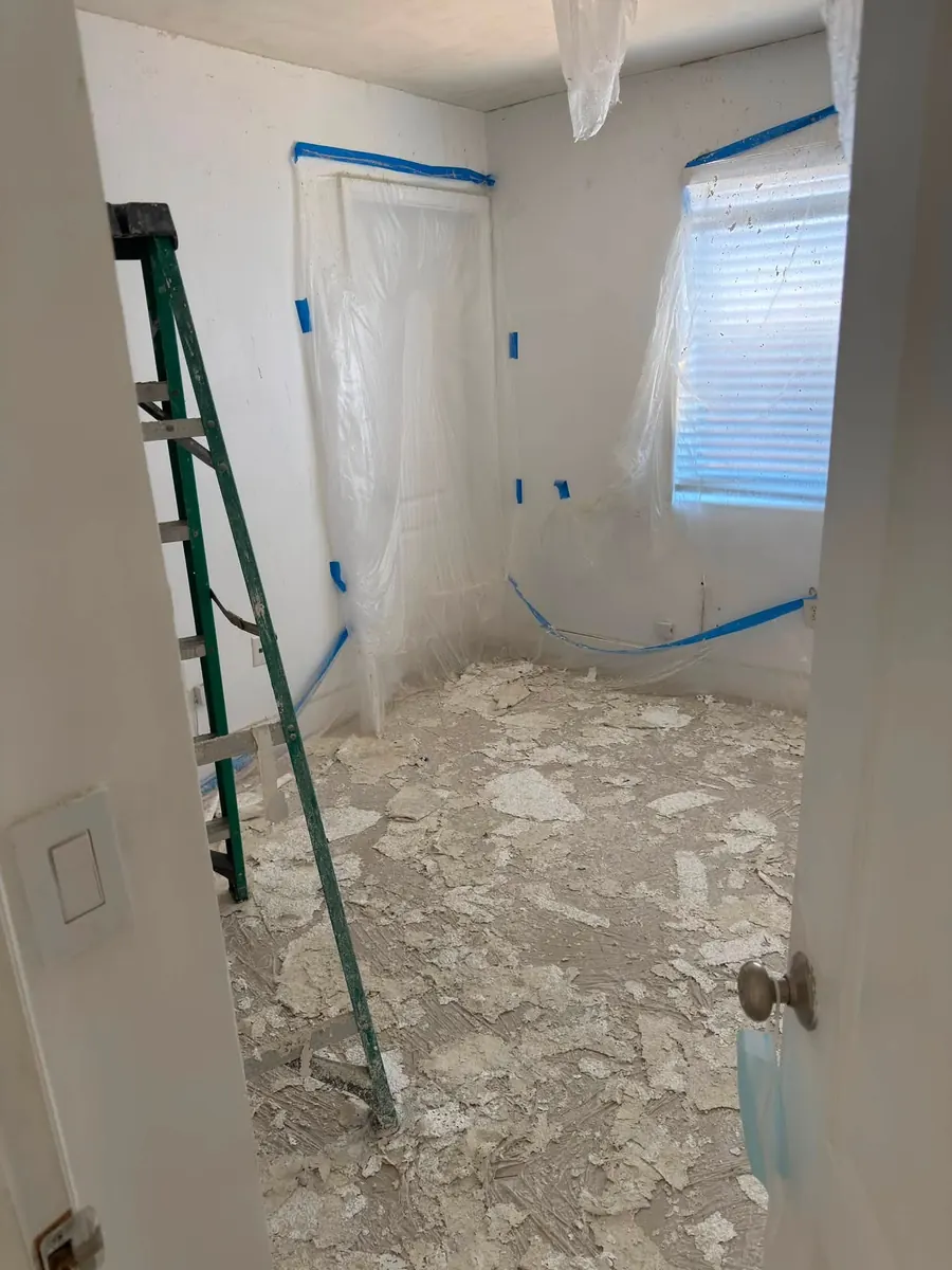 Popcorn ceiling debris on a plastic-covered floor, with the door and window masked off