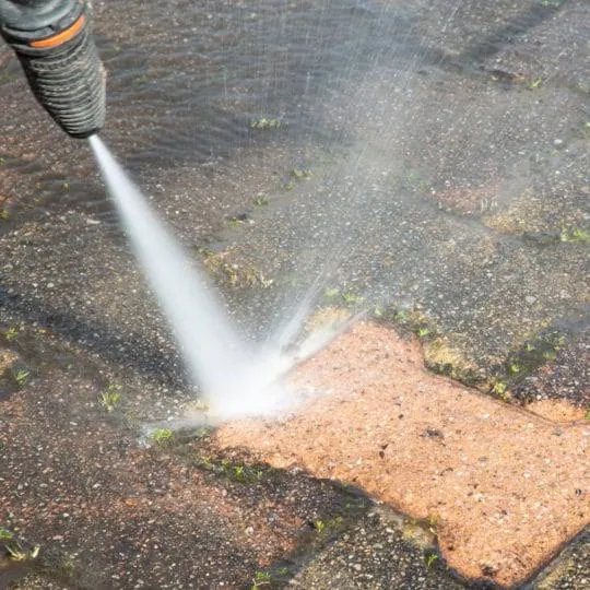 Pressure washer cleaning dirty pavers, showing the clean surface next to the stained area