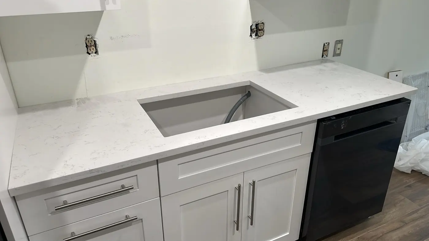 White quartz countertop with an undermount sink cutout over white shaker cabinets beside a black dishwasher