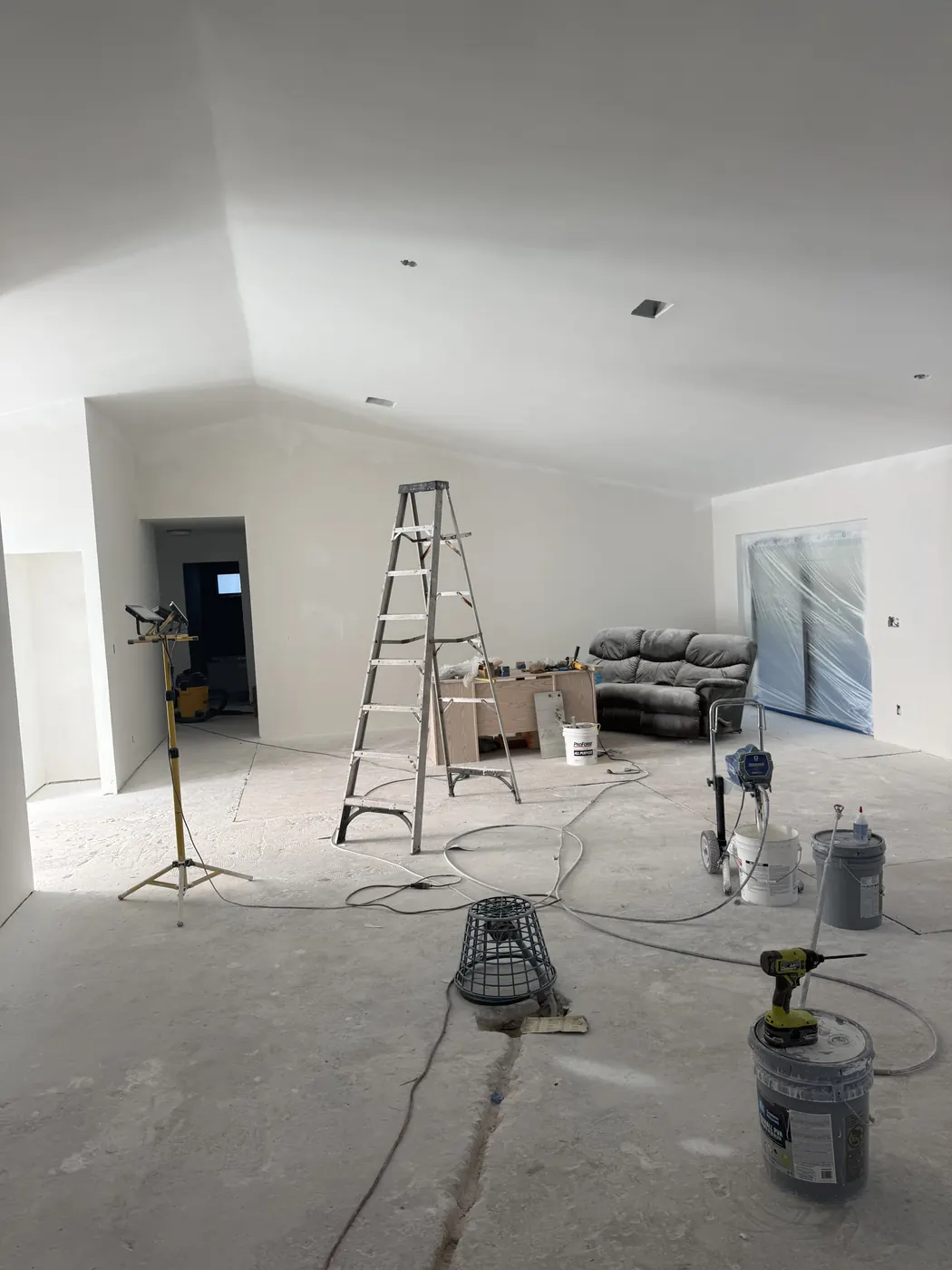 Open living area rebuilt with new drywall on the walls and vaulted ceiling, floors bare and doors masked before paint and flooring