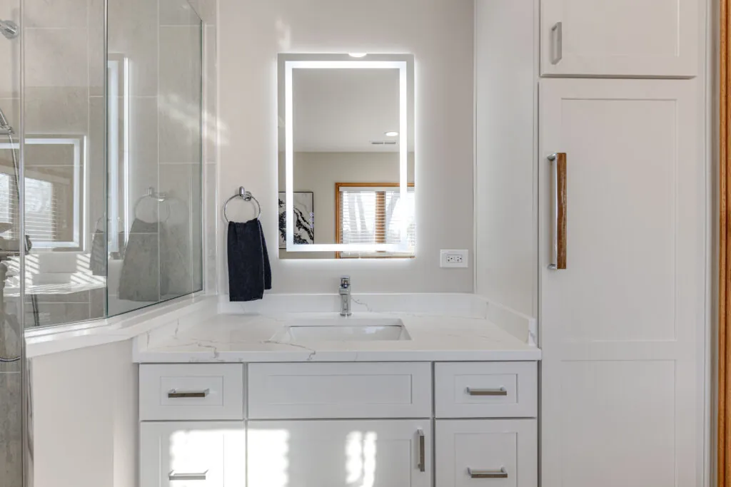 White shaker bathroom vanity with a veined quartz countertop and backsplash, undermount sink and LED mirror