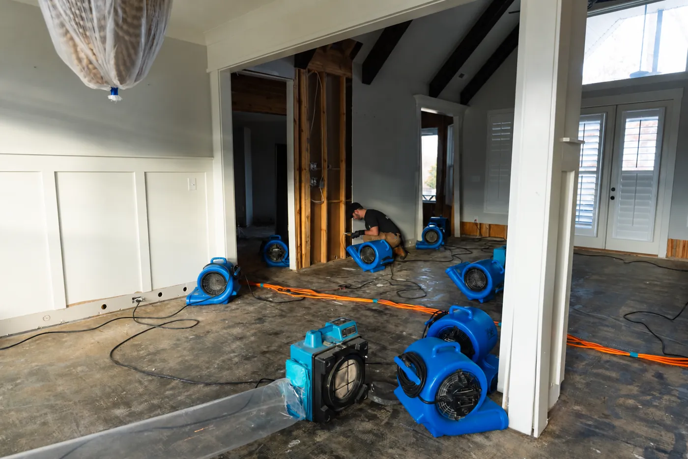Structural drying after water damage: air movers and an air scrubber running while a technician checks opened walls