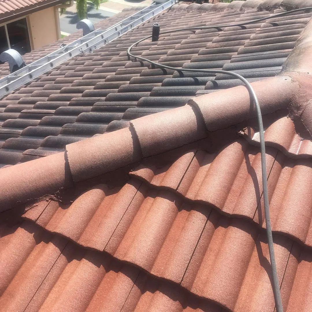 Clay tile roof mid-cleaning, with cleaned tiles below the ridge and dark, mildew-stained tiles above it