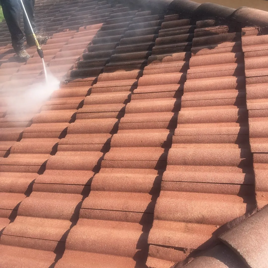 Technician pressure washing a clay tile roof, with the cleaned red tiles beside darker tiles still covered in dirt and mildew
