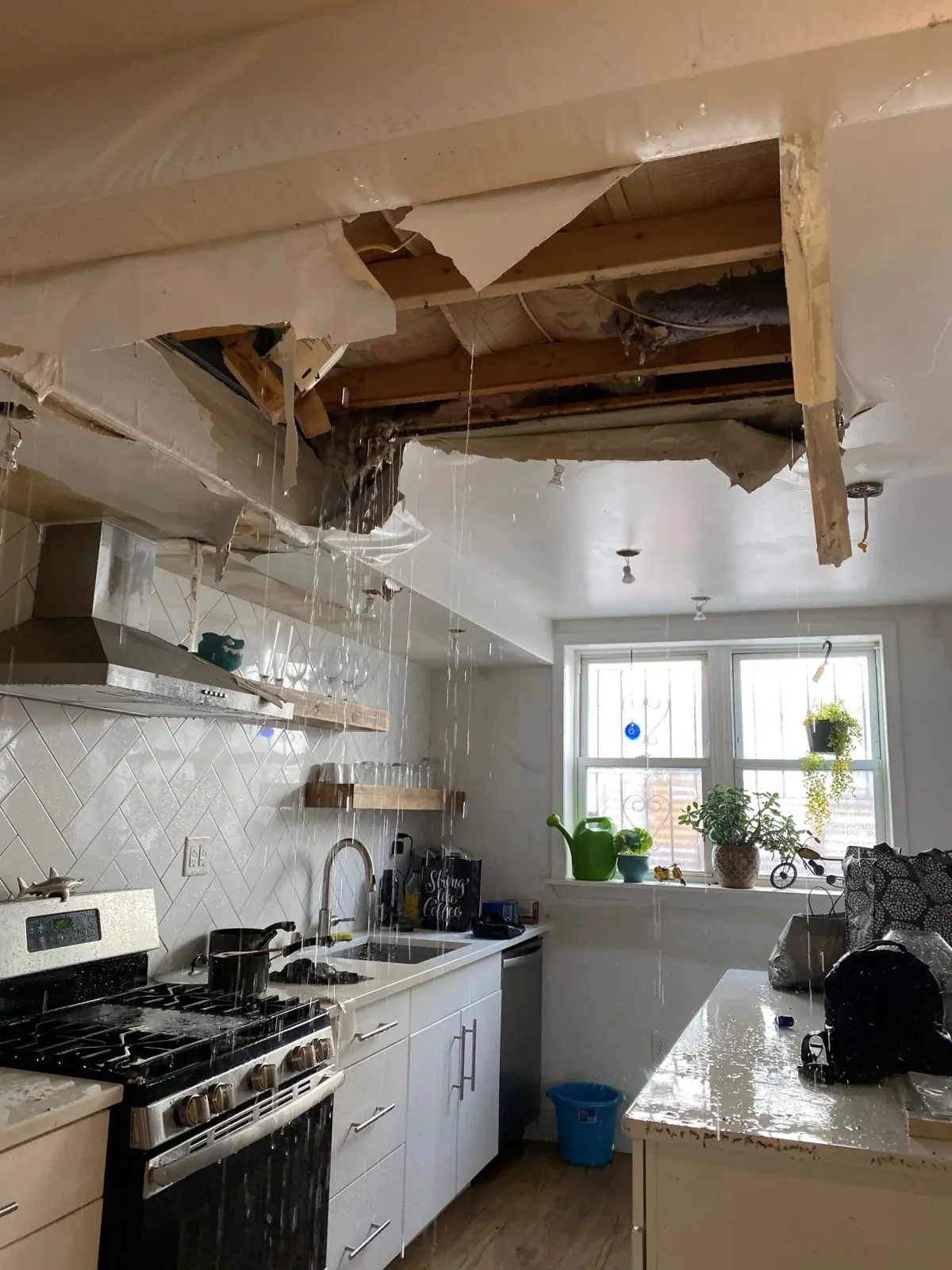 Kitchen ceiling collapsed by an active water leak, with water pouring onto counters and appliances