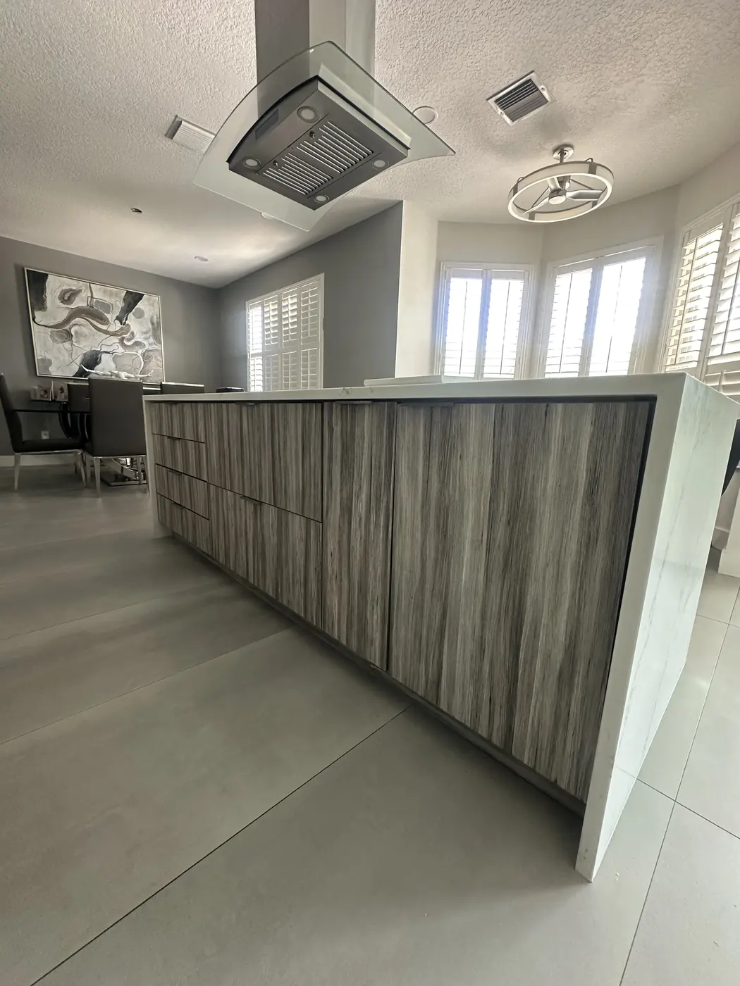 Kitchen island with wood-grain slab cabinets and a white quartz waterfall edge running down to the floor, under a glass island hood