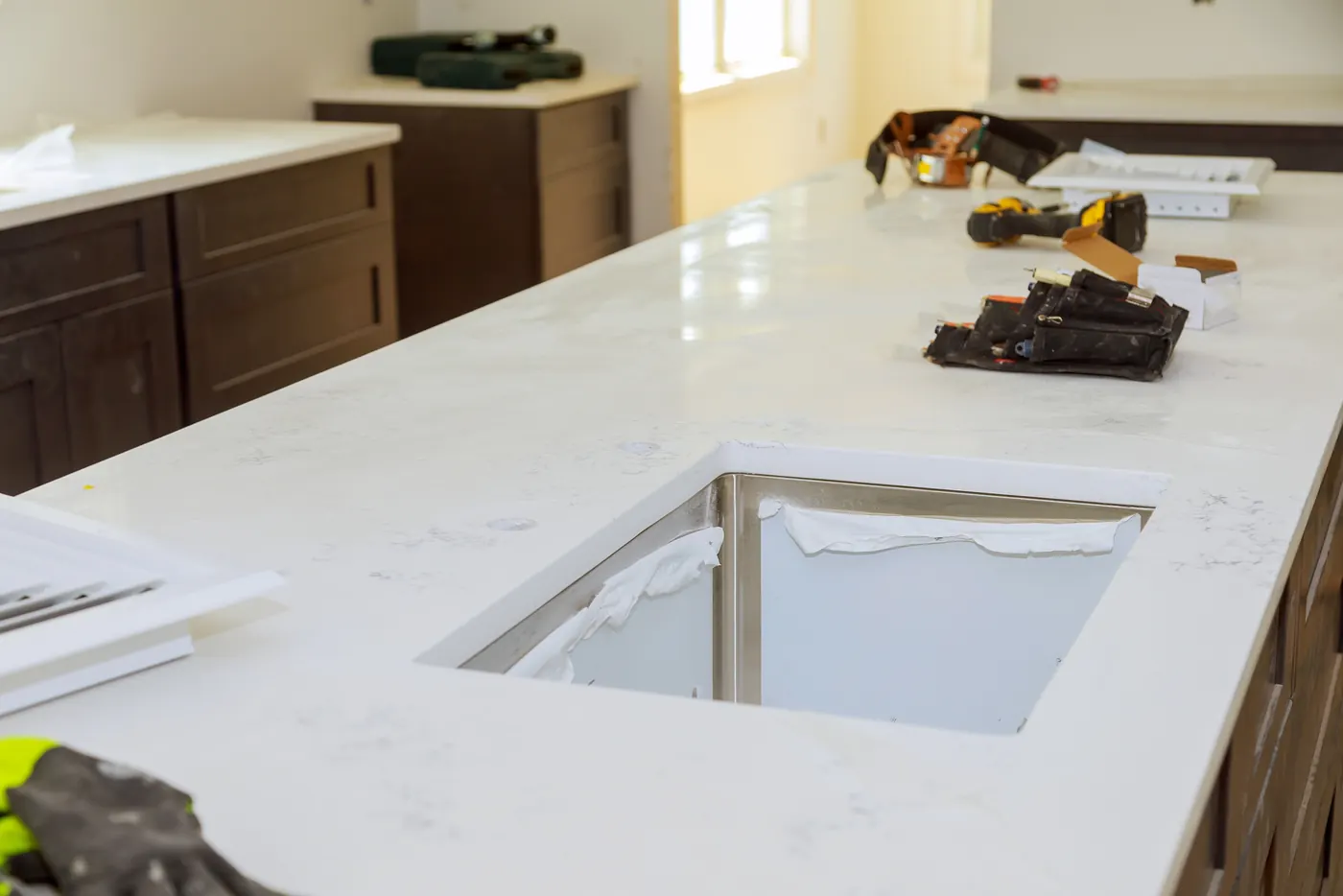 White quartz countertop with an undermount stainless sink being installed over dark shaker cabinets