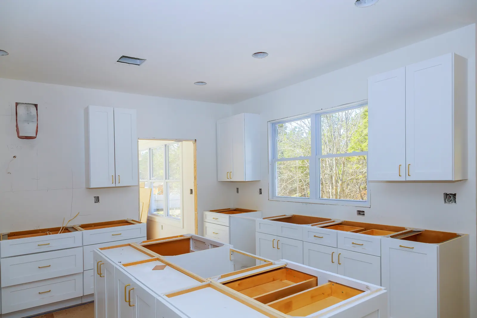 Kitchen remodel in progress with white shaker cabinets, gold hardware and a large island being installed