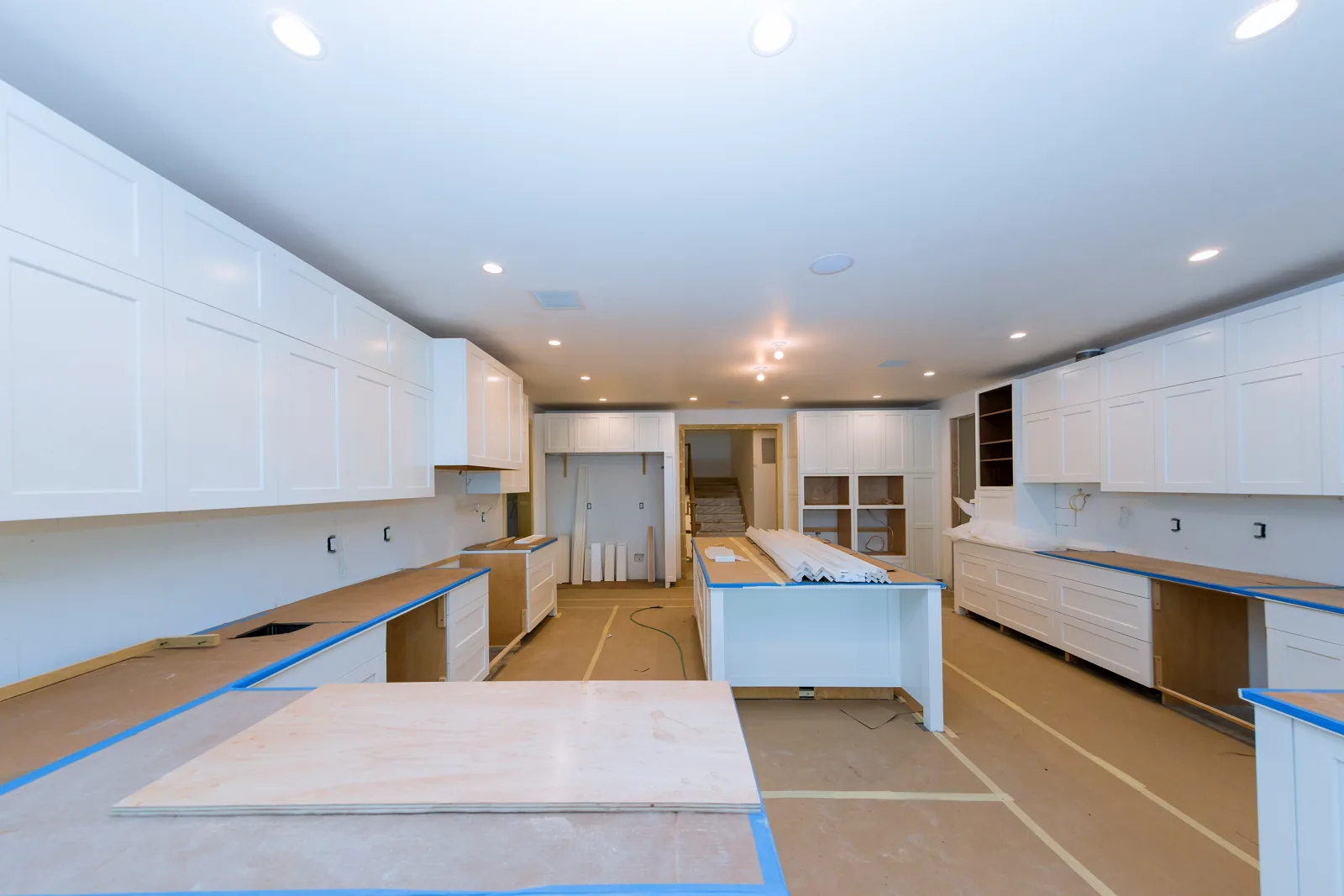 New white shaker kitchen cabinets and island being installed, with countertops protected and floors covered