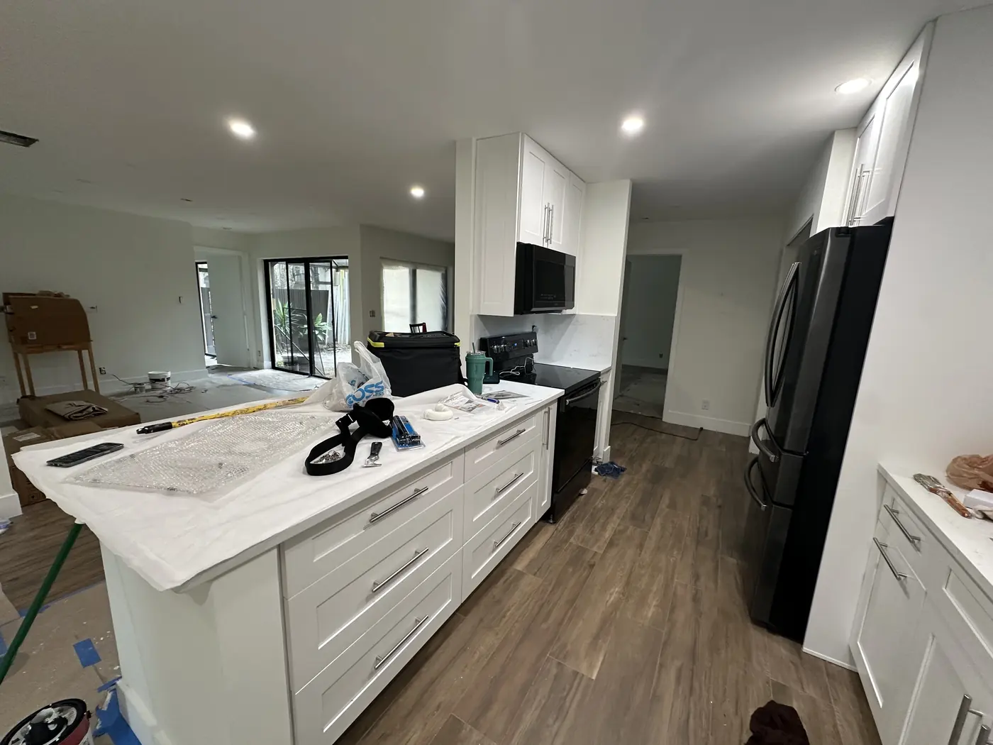 Open kitchen with a white shaker island and quartz countertop, black range and microwave, and wood-look tile floor