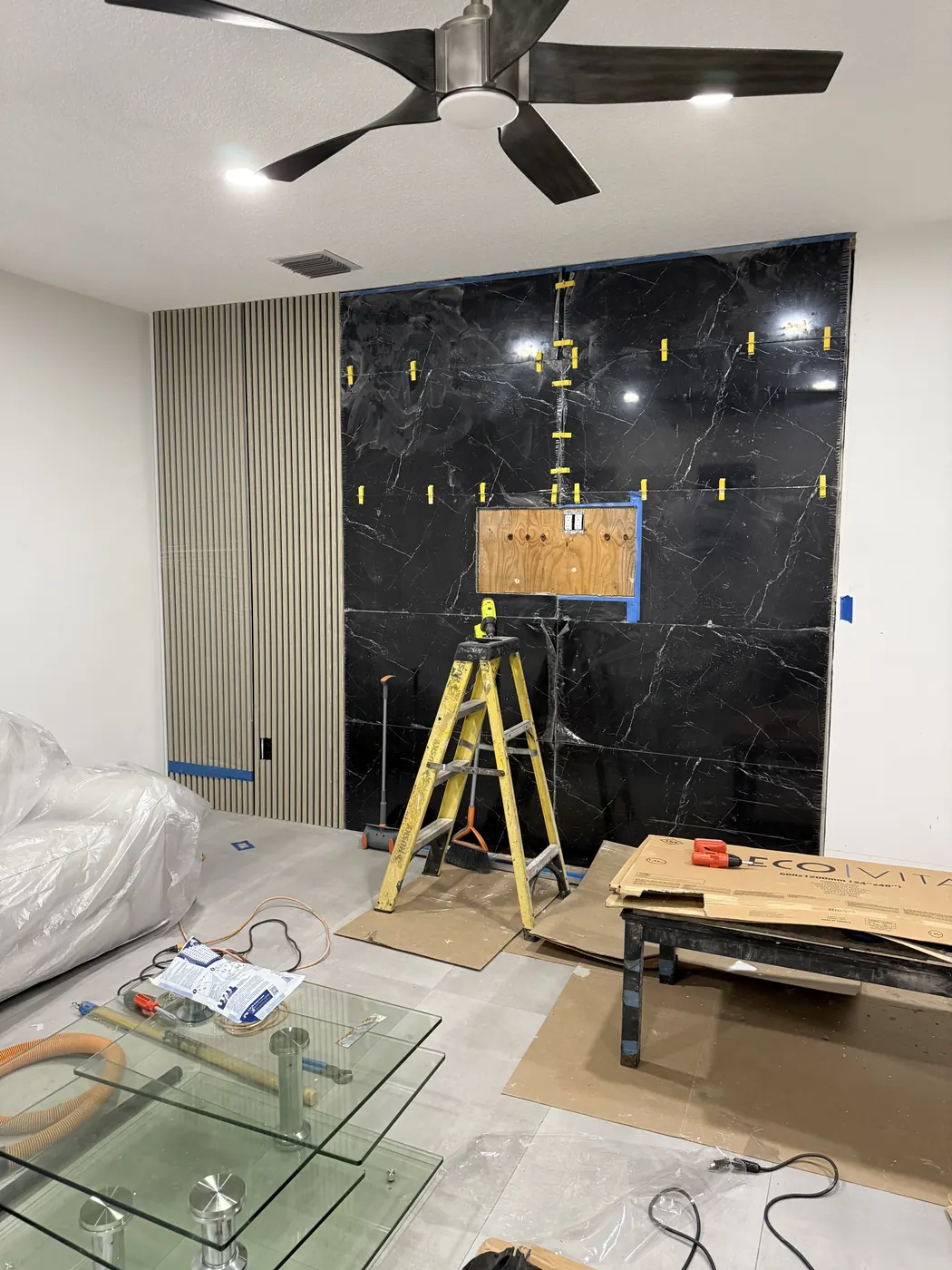 Wood slat panels installed beside the black tile wall, with floors and furniture protected